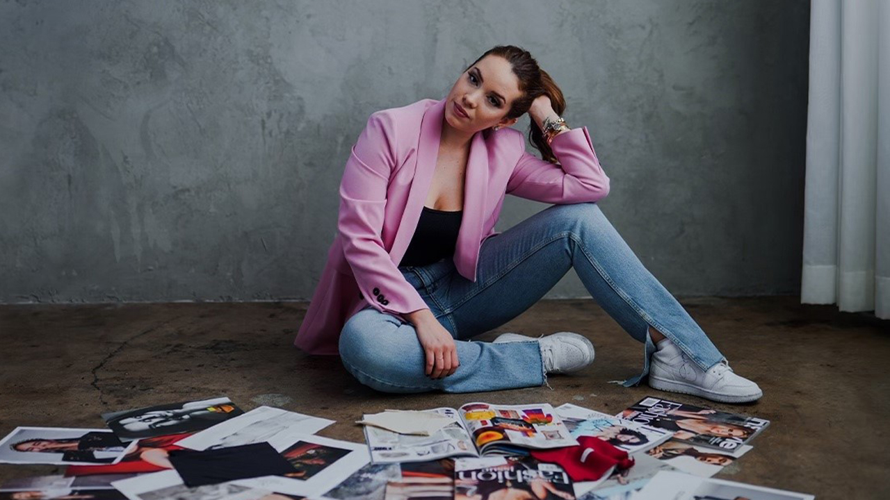 Photo of Natasha Pavlica in pink blazer and jeans on floor behind several fashion magazines scattered on the floor