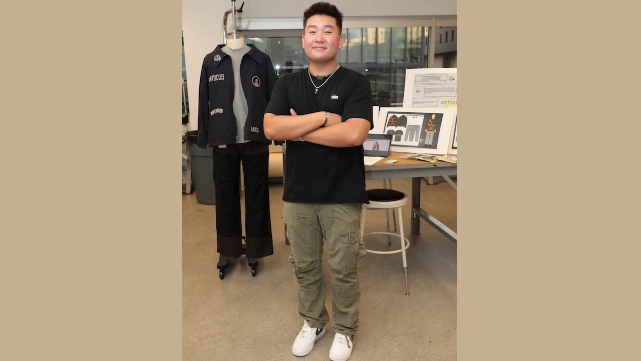 FIDM Grad Colin Huang stands with his arms folded in front of his menswear designs