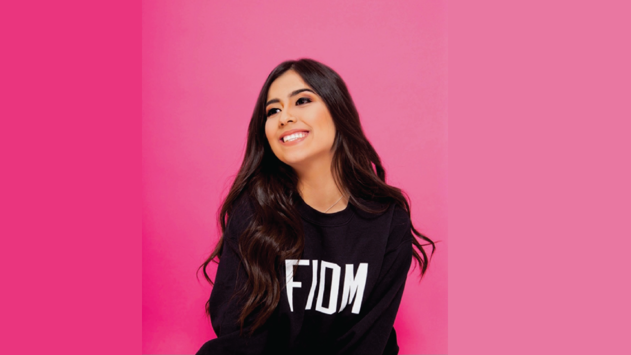 FIDM Graduate Alyssa Chavez smiles in a FIDM sweatshirt against a pink background