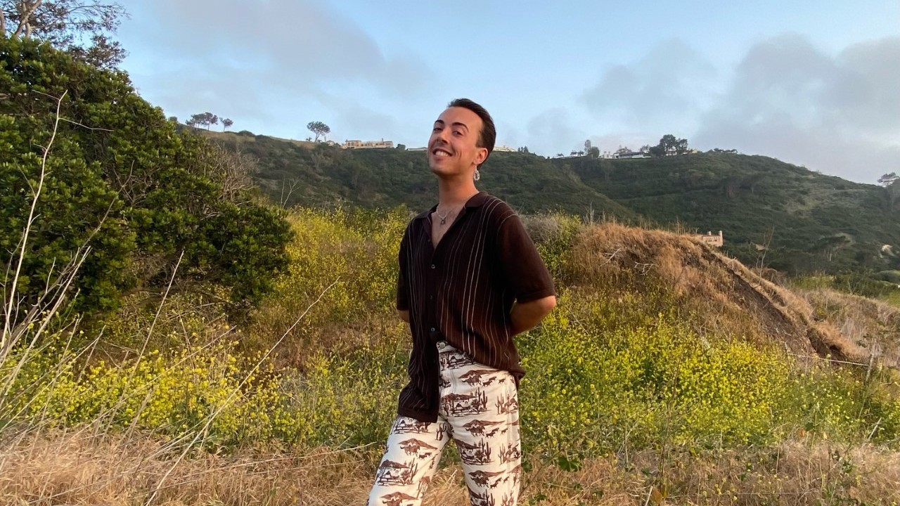 Cameron Harp stands, smiling, on a hillside with wildflowers
