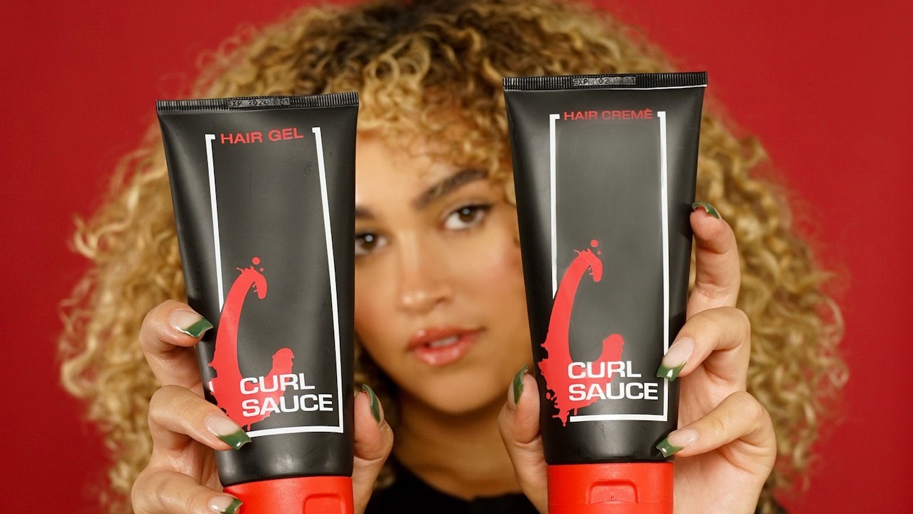 Grad Tala Othman holds two bottles of her curly hair product Curl Sauce against a red background