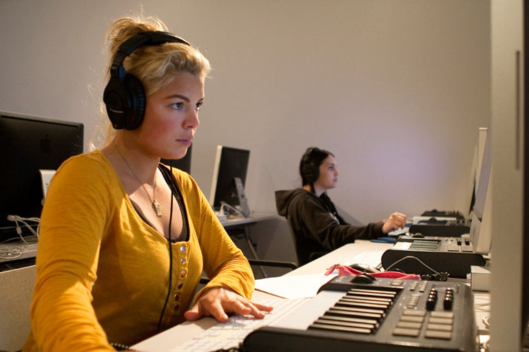 A student wearing headphones scores her video at an audio workstation