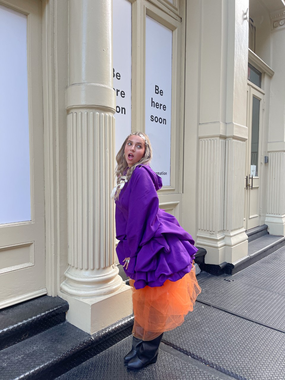 FIDM Student Lexy Silverstein wearing a purple jacket and orange skirt standing outside on a city sidewalk