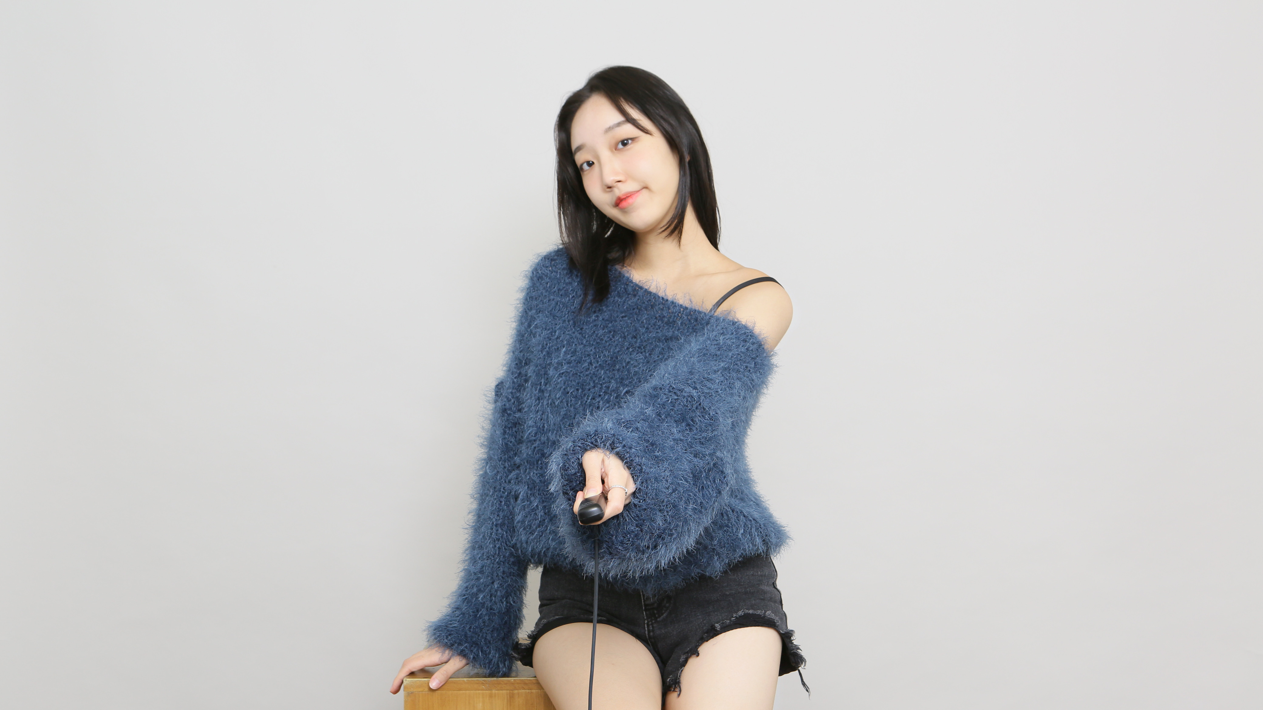 FIDM Fashion Design Student HyeRin Lee wearing a fuzzy blue off the shoulder sweater and black shorts as she tilts her head and points at the camera