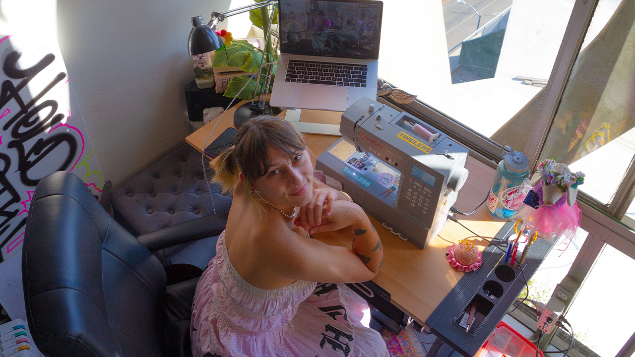 Overhead photo of Analeia Bella Madden in pink strapless dress sitting at her desk with a sewing machine in front of a large window