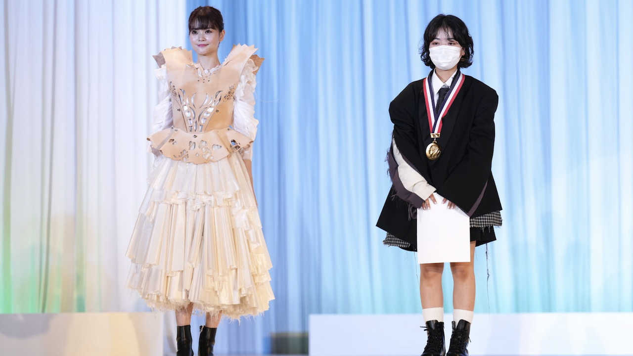 A runway photo of a model wearing the UEDA fashion design winner's design next to designer Ayumi Takahashi