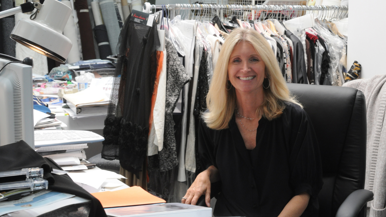 fashion designer Karen Kane sits at her desk with a rack of clothing behind her