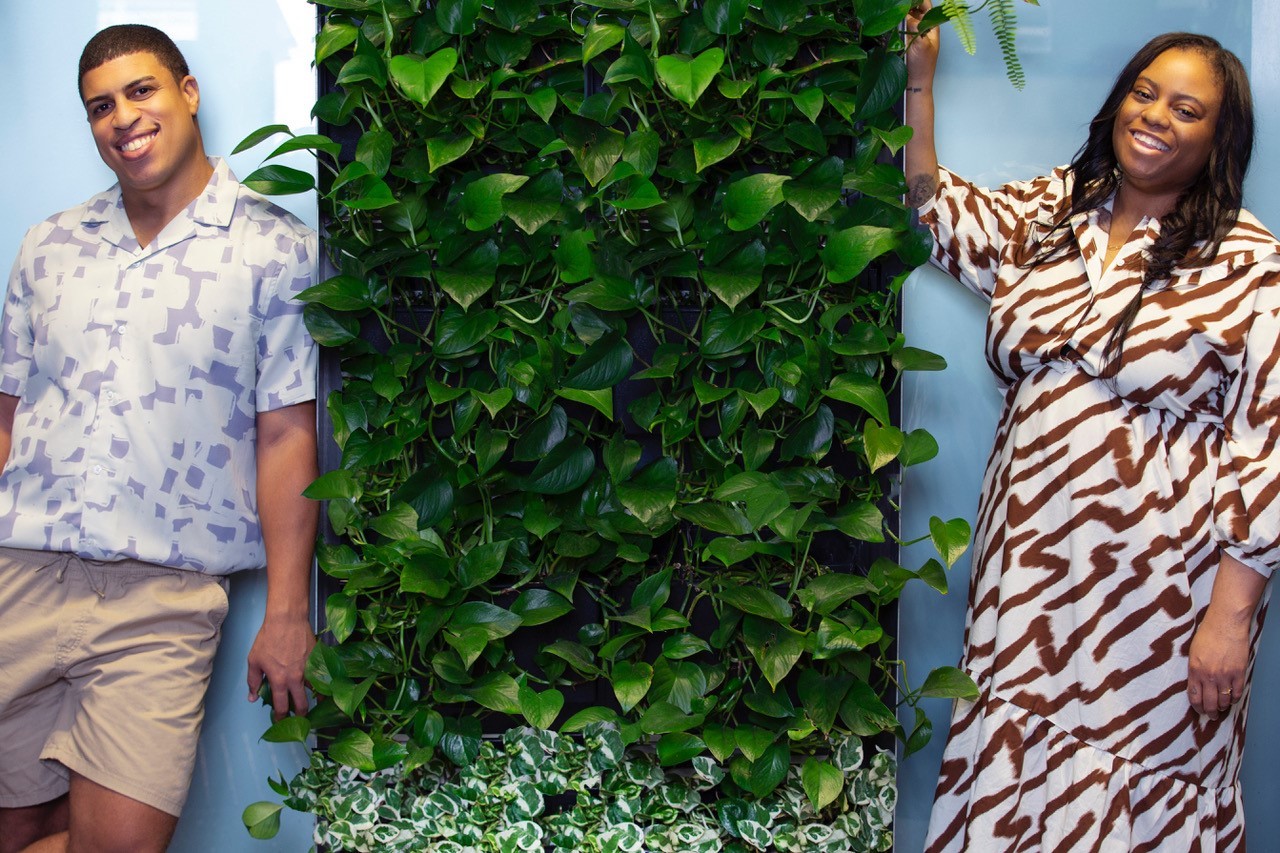 FIDM Grads Tyree Robinson and Audrey Brianne pose next to a plant wall