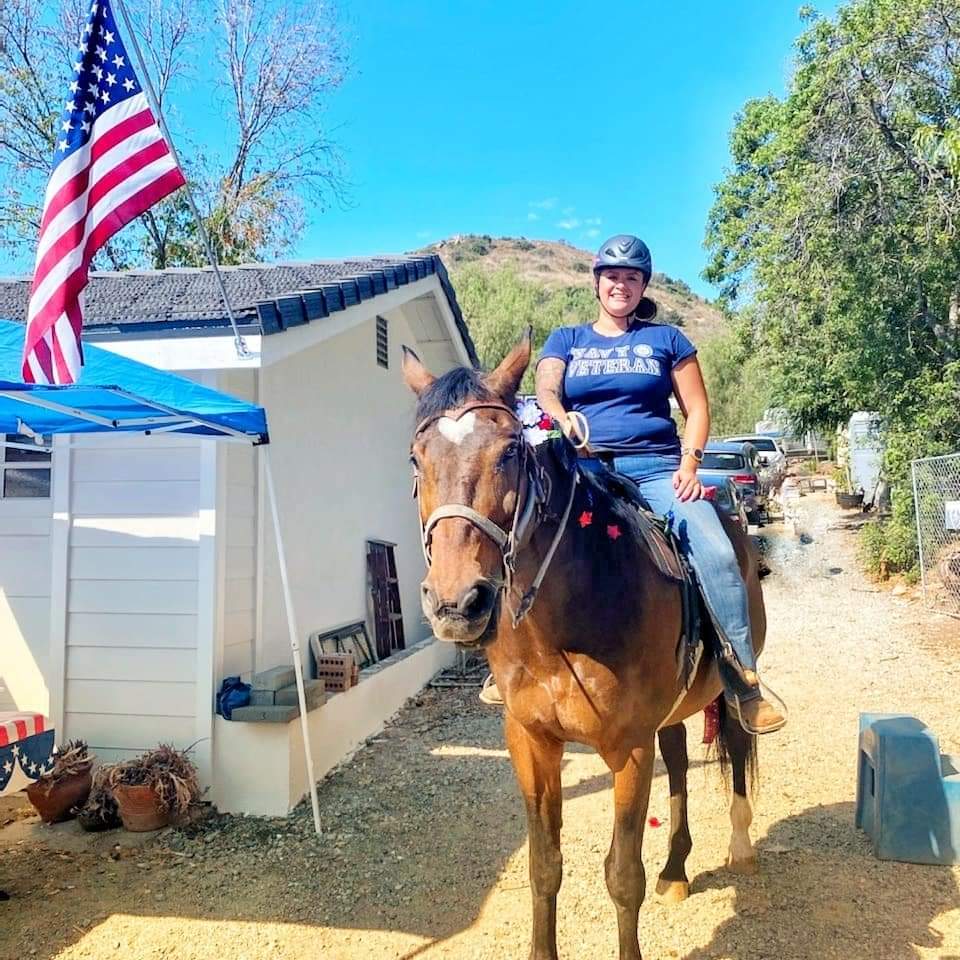 Jessica Mirazo rides a horse as she wears a t-shirt with the text Navy Vet on the front