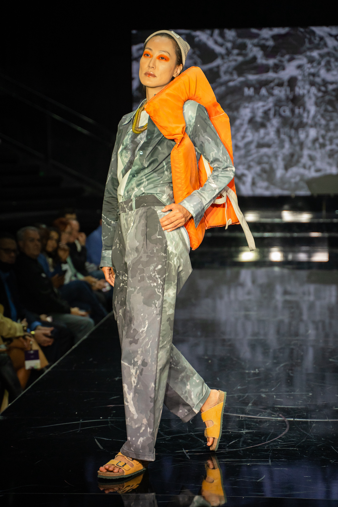 A model walks the runway in an ocean-inspired shirt and pants accessorized with an orange life vest on the shoulder