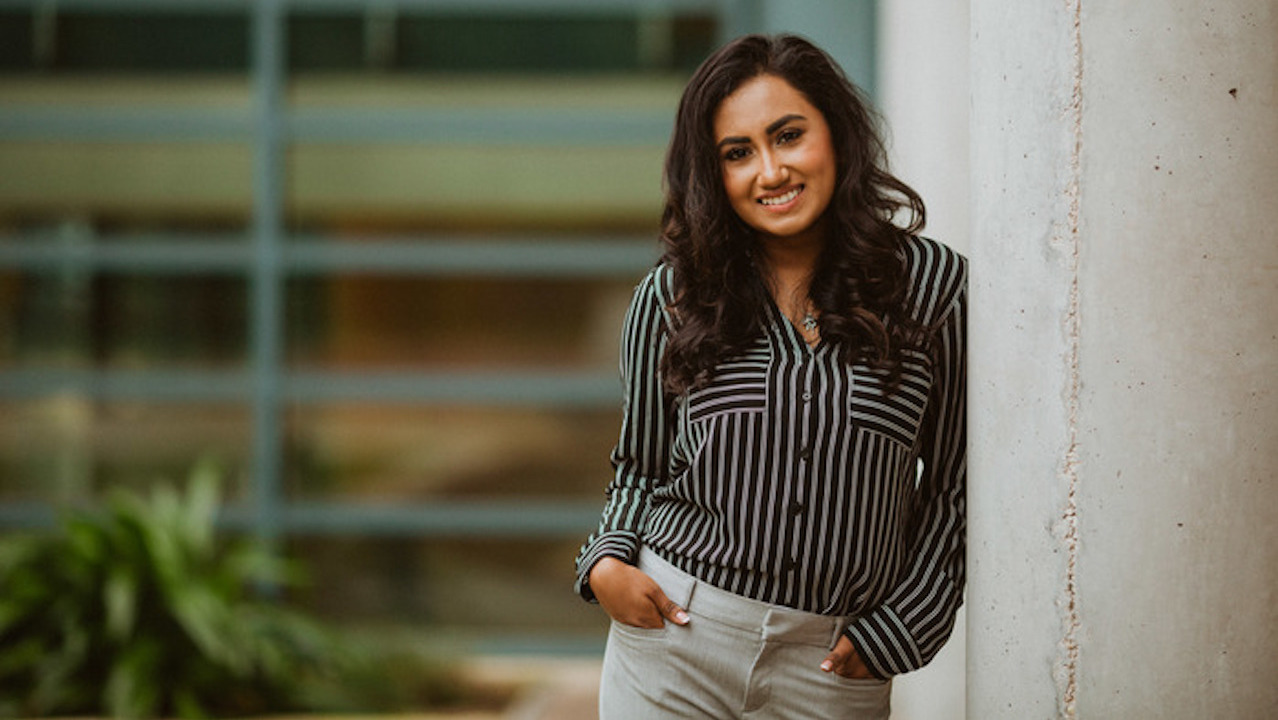 A photo of FIDM Graduate Amulya Deva smiling and leaning against a wall