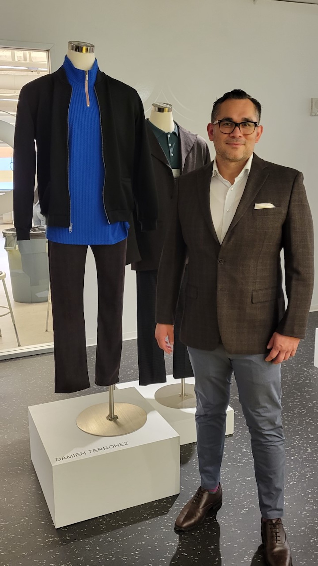 FIDM Graduate Damien Terronez stands next to his menswear designs