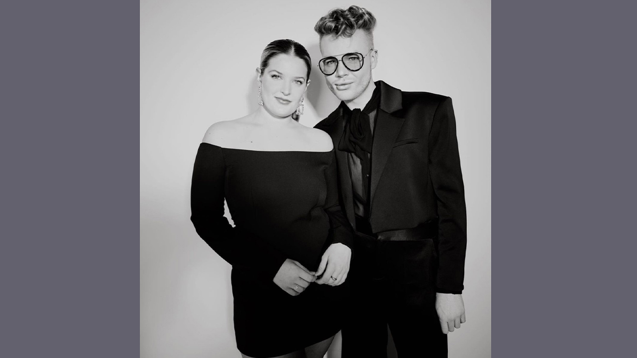 Black and white photo of Hannah and Matthew. Hannah wears a black off shoulder dress and Matthew wears a black suit.