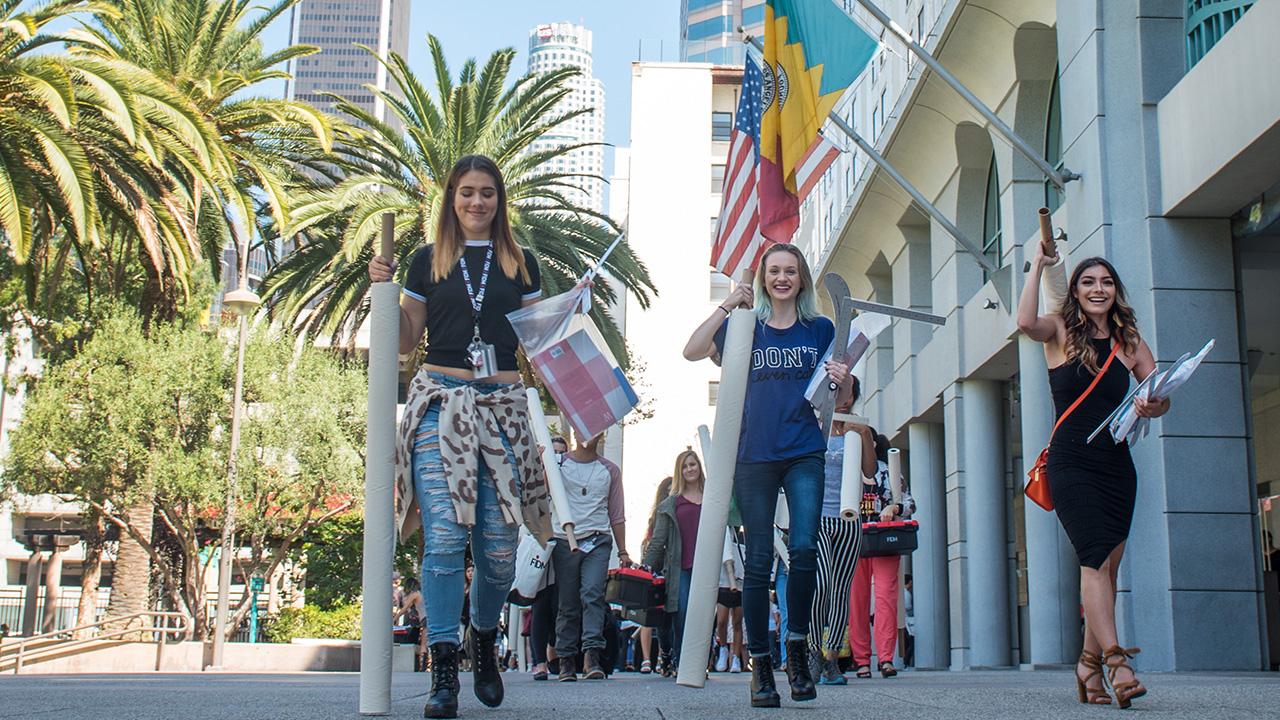Student walk to class carrying bolts of fabric in front of FIDM Los Angeles
