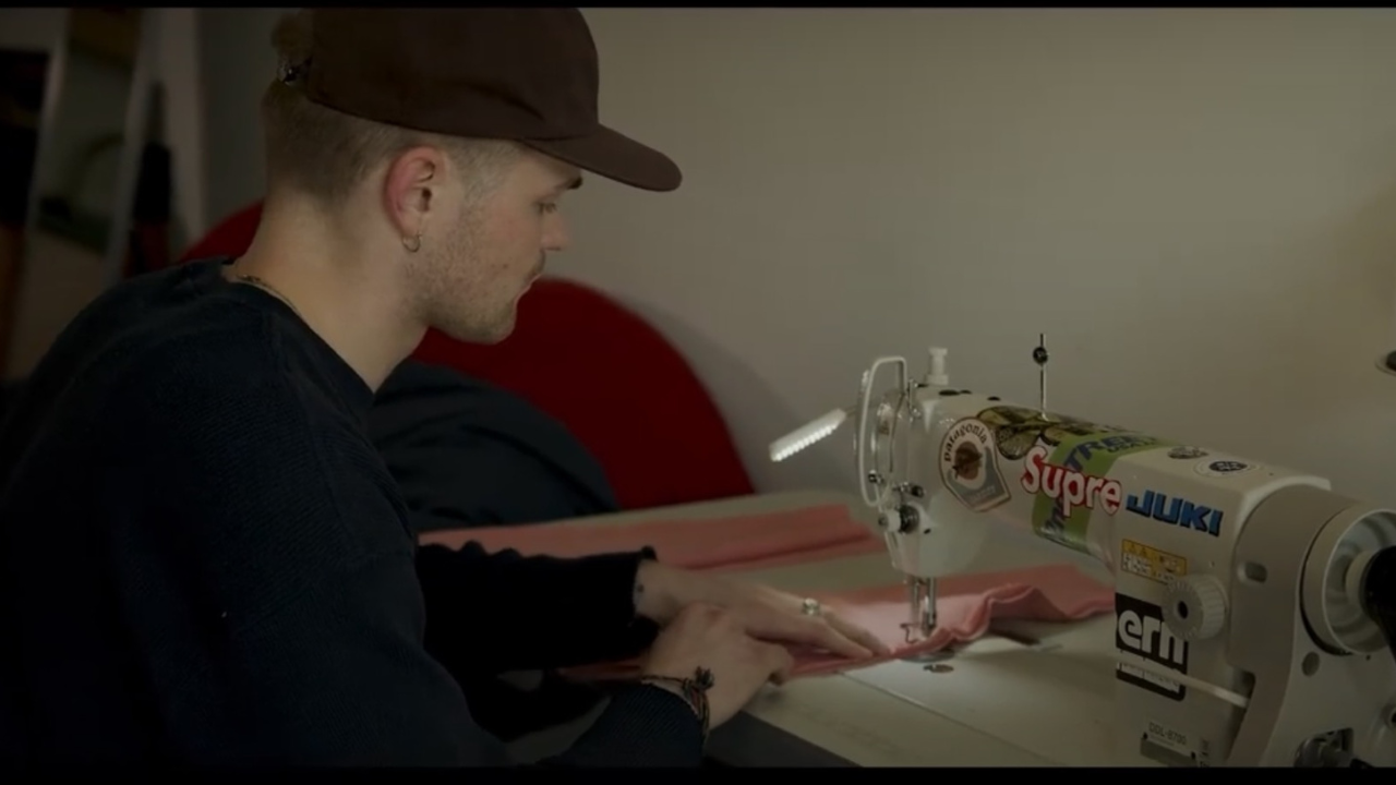 Alexander Novak wearing a baseball cap sewing on a sewing machine indoors
