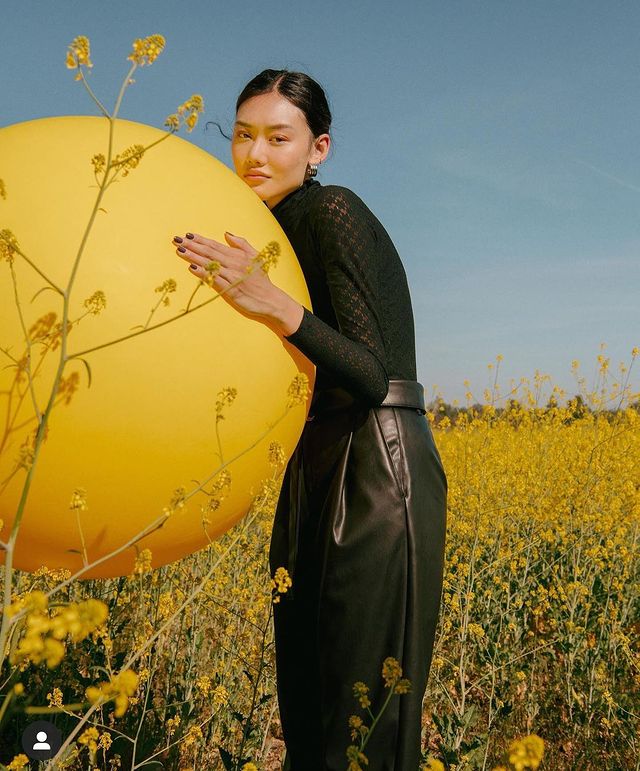 model holding a large yellow ball standing outside in a field