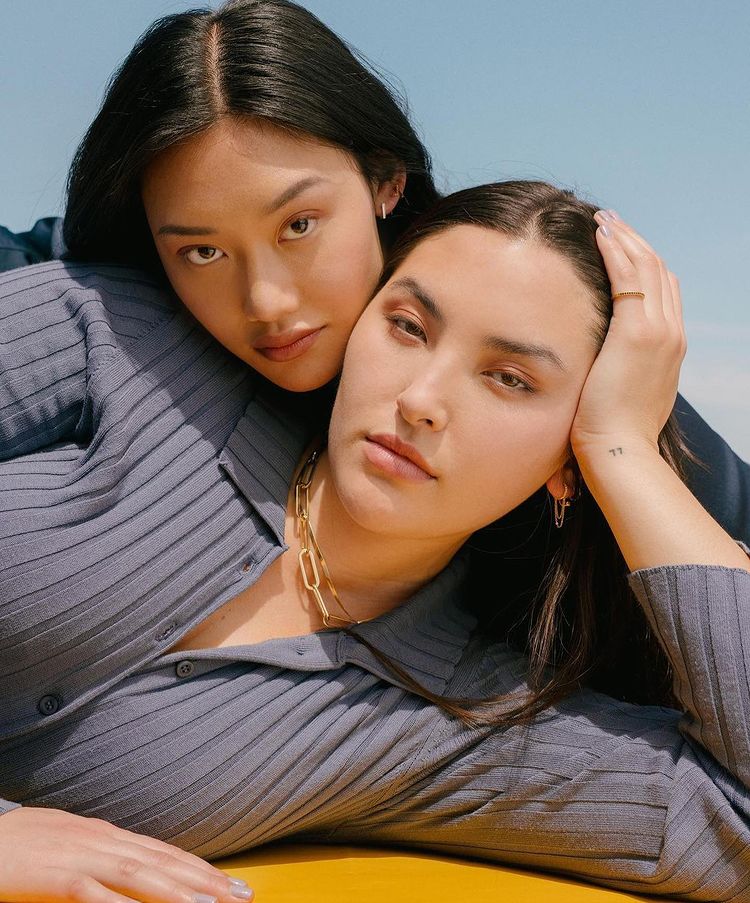 two female models wearing sweaters laying on the ground