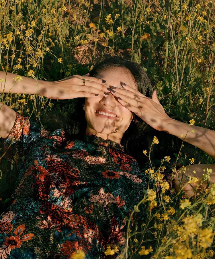 model laying in a field of flowers covering her eyes with her hands