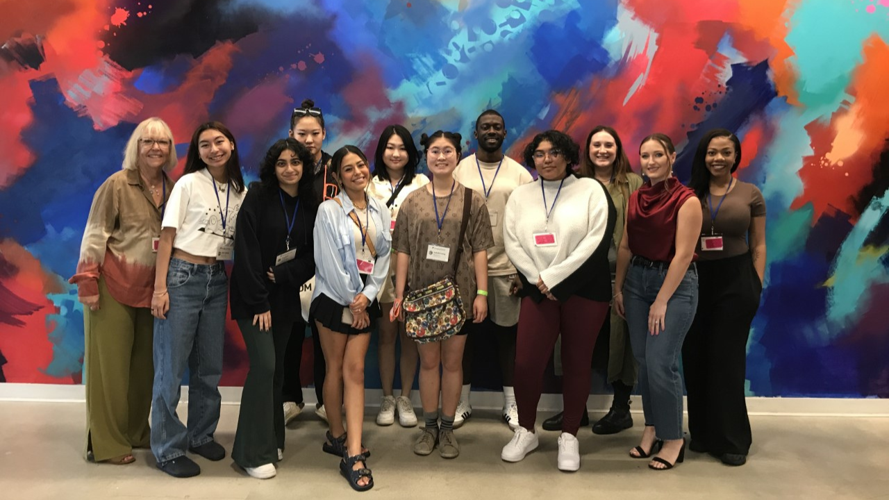 FIDM students indoors at Fabletics headquarters standing against a colorful wall of swirls of blue red orange and light green