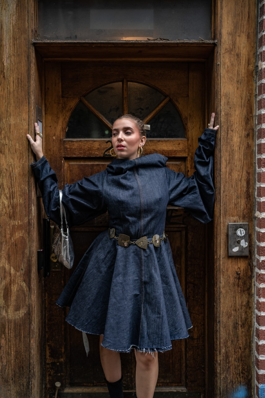 FIDM Student Lexy Silverstein wearing an all denim dress standing in a wooden doorway on the street