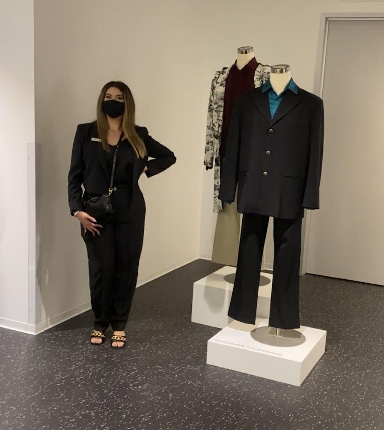 FIDM Graduate Rosemarie Ravenwood poses in a mask next to her menswear designs