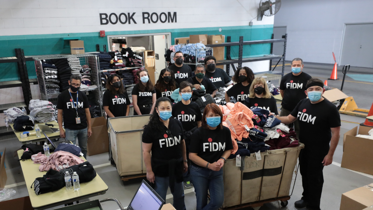 FIDM Employees in black FIDM T-shirts standing indoor next to boxes of merchandise