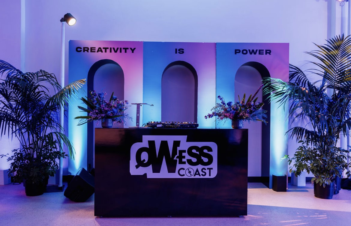 A DJ booth flanked by large plants and colorful lights designed by Susan Houmes