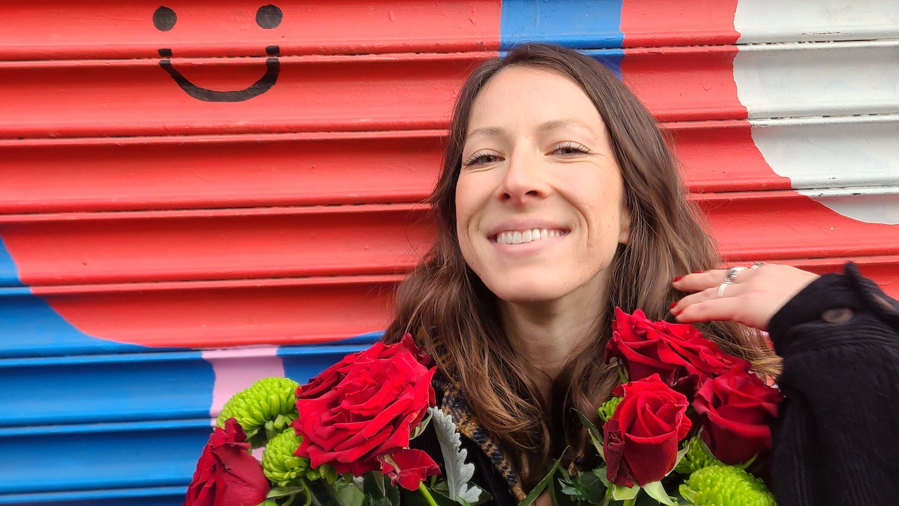 Kelli Burt smiles against a red and blue background holding red roses