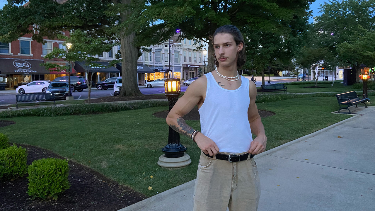 Photo of Tyson Wilson in white tank and khaki pants with hands on hips looking to his right in a city park