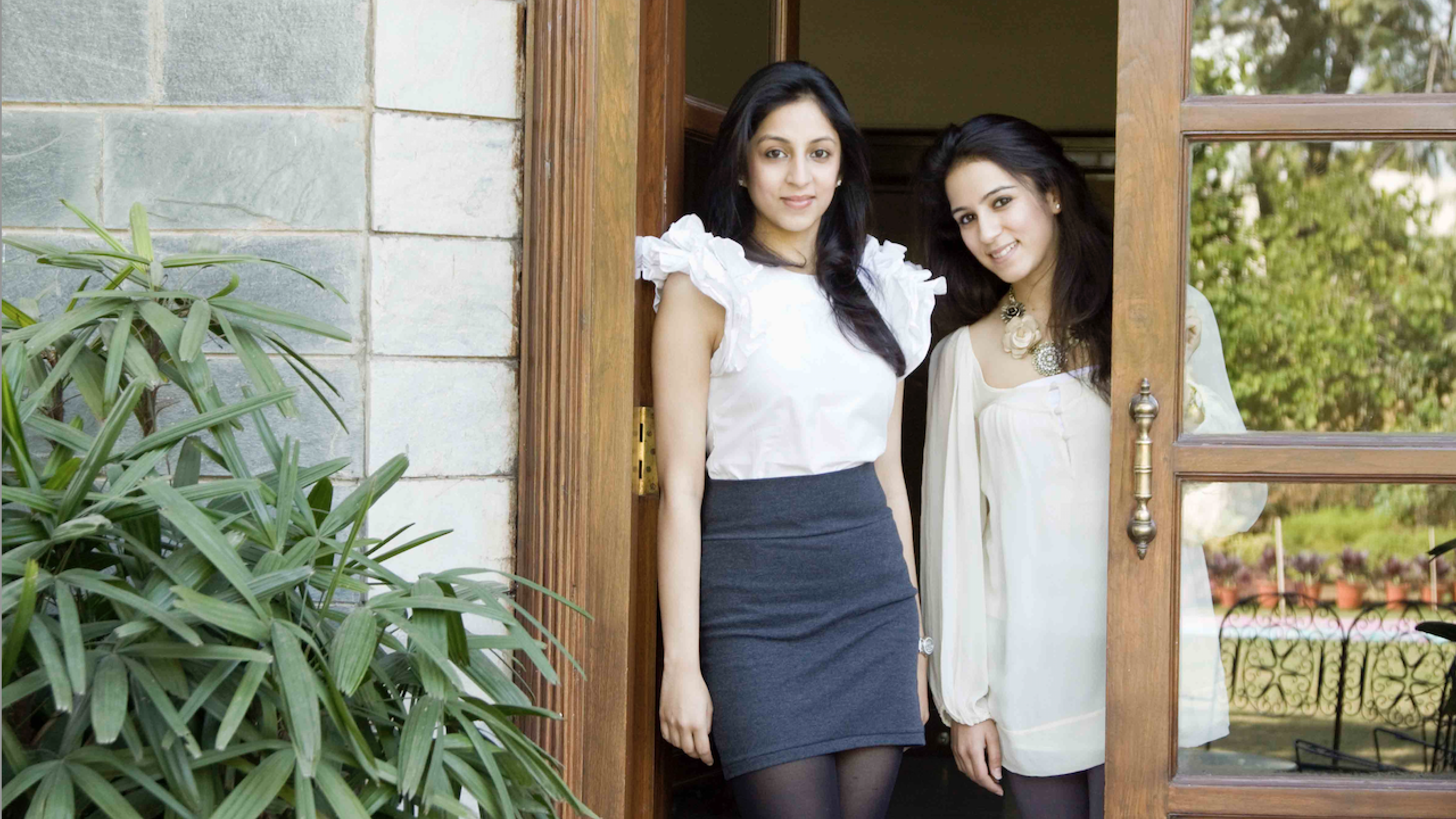 Sisters and FIDM Grads Radhika Mittal and Madhvi Pittie stand in a wooden doorway