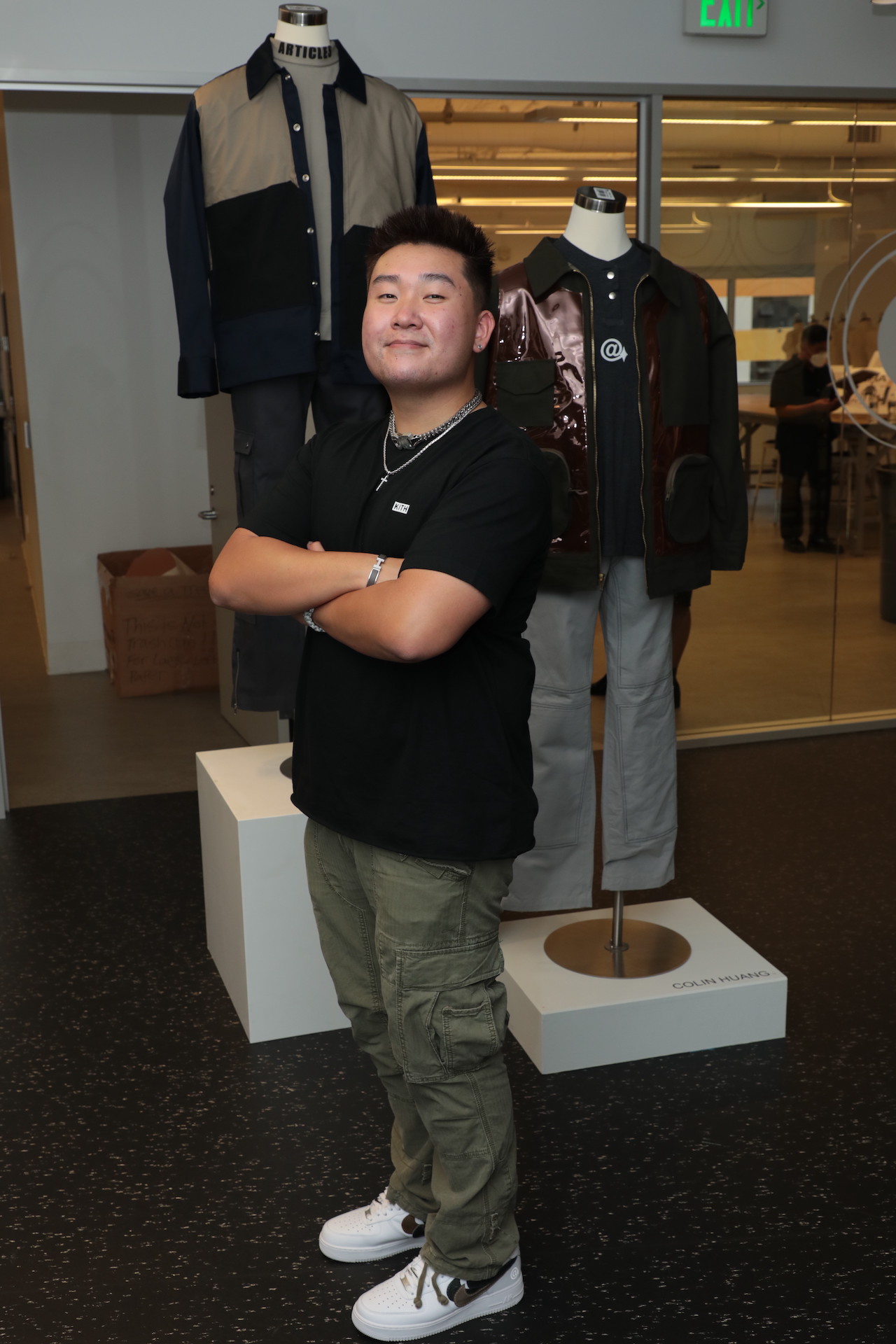 FIDM Grad Colin Huang stands in front of two of his menswear designs