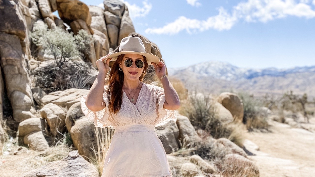 A portrait of Sara Lashkari wearing a hat and sunglasses in a desert landscape